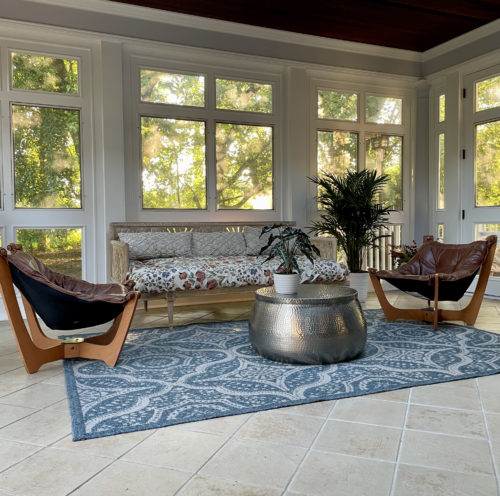 Living room with round grey coffee table surrounded by plants and beautiful forest backdrop